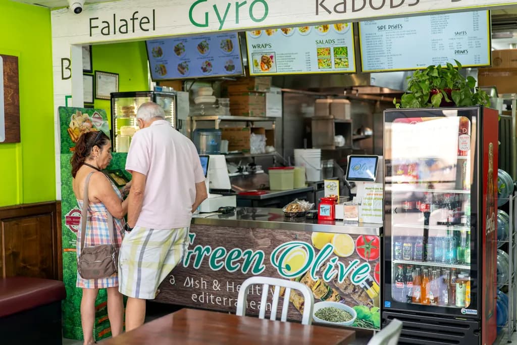 Guests ordering at The Green Olive counter under the Falafel, Gyro and Kabobs menu boards