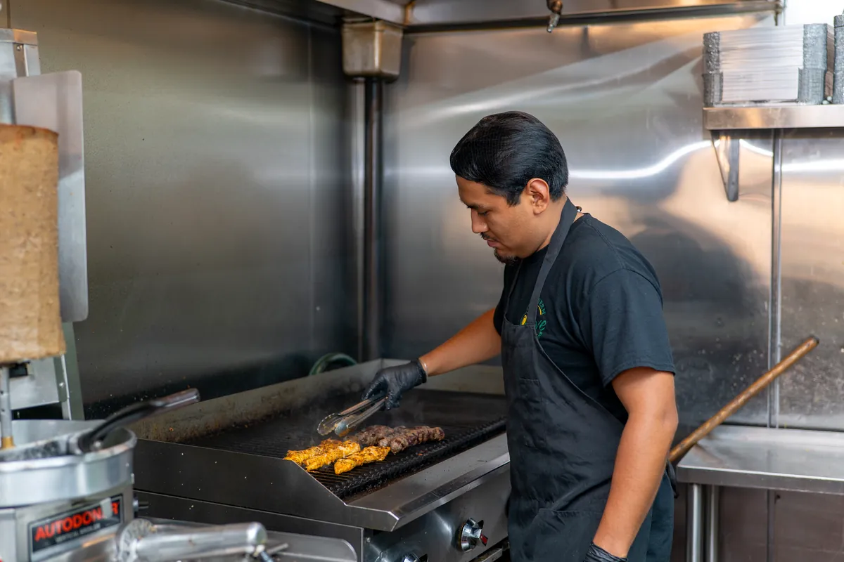 A Green Olive cook grilling chicken and kafta kebabs