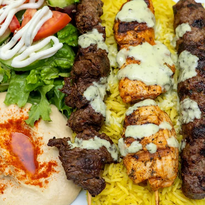 Mixed grill plate: chicken, steak and kofta kabobs over rice with hummus and salad