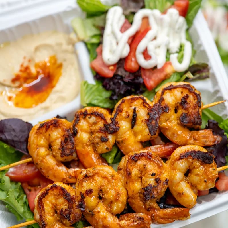 Two grilled shrimp skewers over salad with hummus